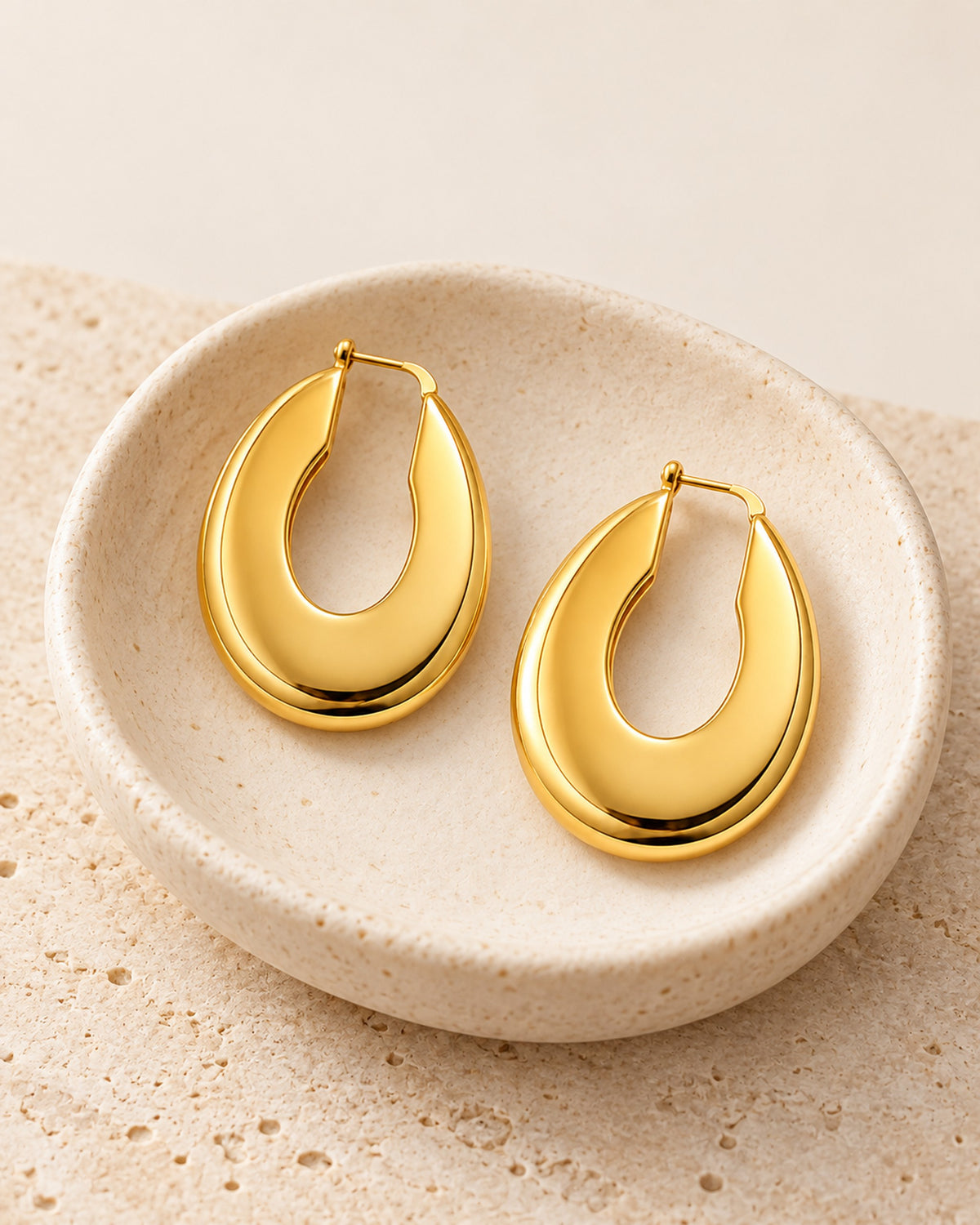 Aurélie sculpted oval hoop earrings in Gold, still life on travertine