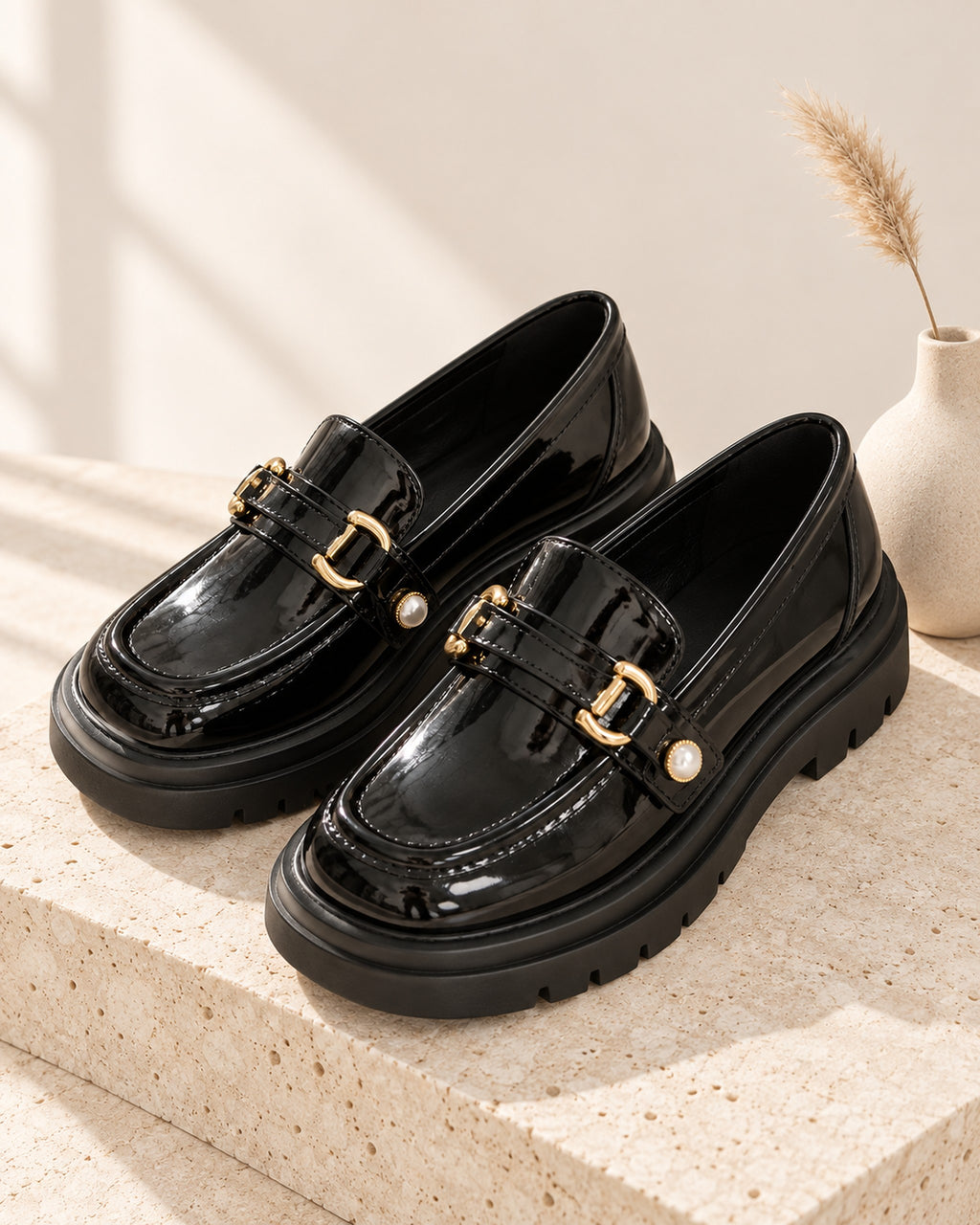 Bérénice patent-finish platform loafer with horsebit buckle in Black, still life on travertine