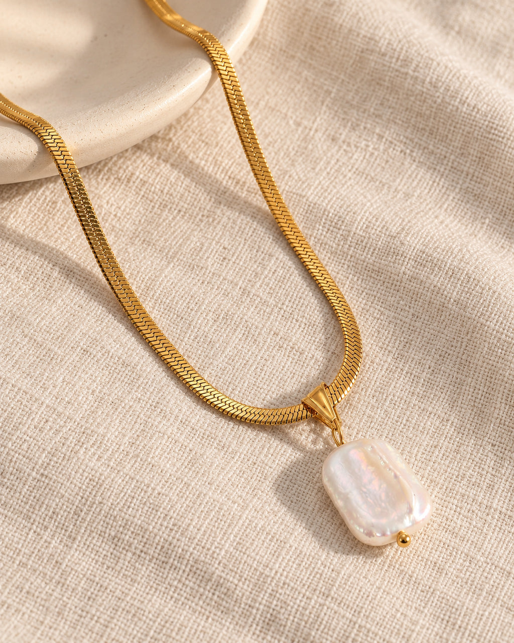 Celeste gold-tone herringbone chain necklace with baroque pearl drop, still life on linen