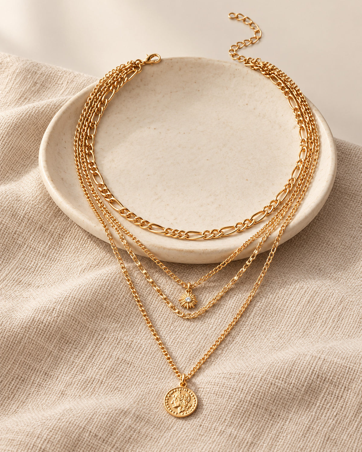 Colette four-strand layered necklace with sun charm and coin medallion in Gold, still life on linen