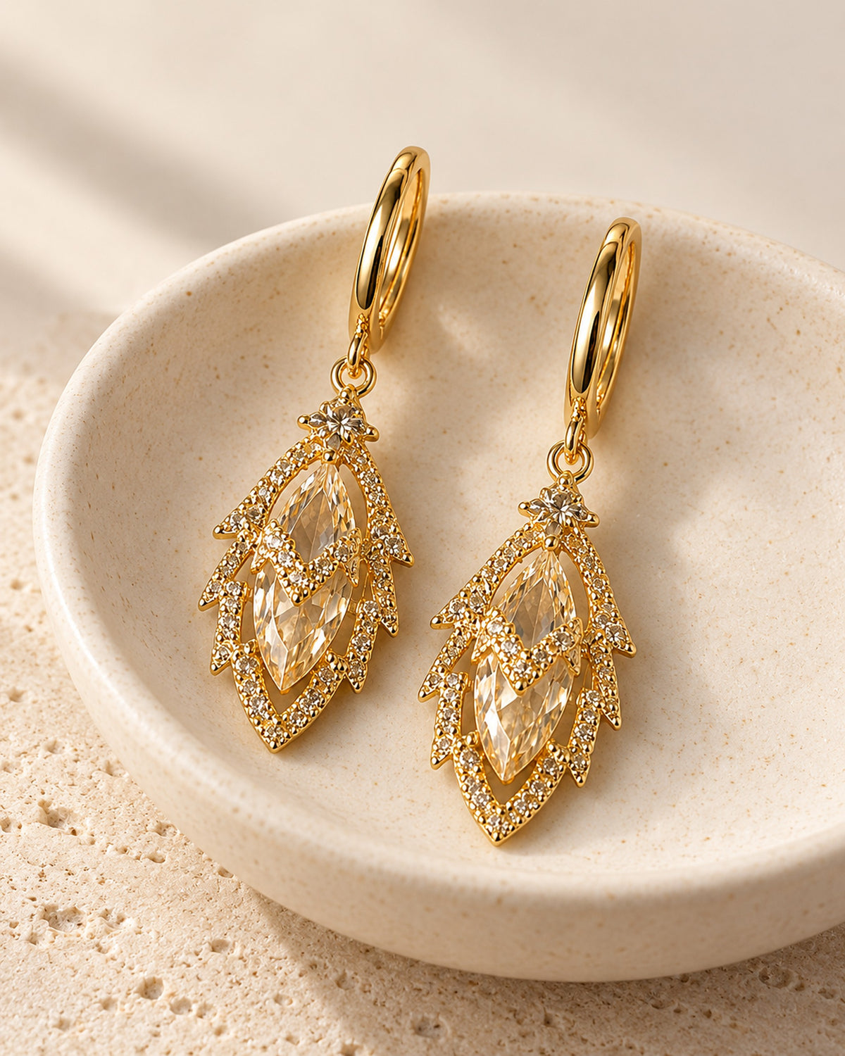 Iris zircon leaf drop earrings on gold-tone huggie hoops in Gold, still life on travertine