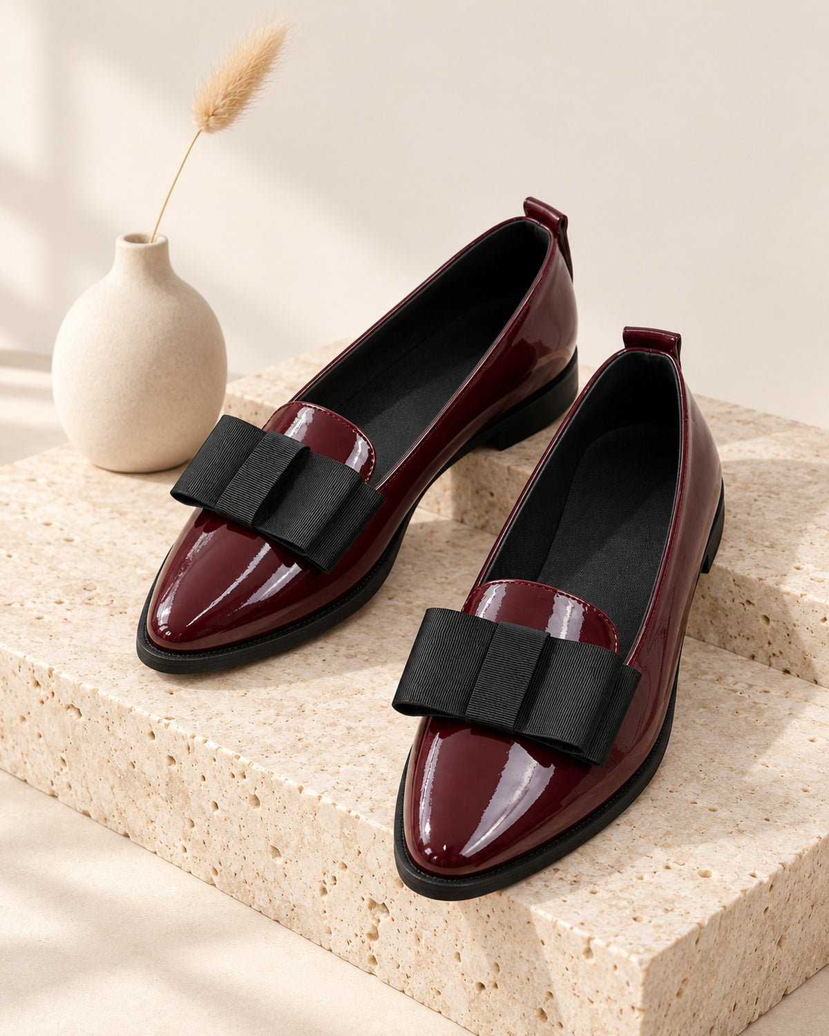 Léa patent-finish pointed ballet flat with oversized bow in Burgundy, still life on travertine