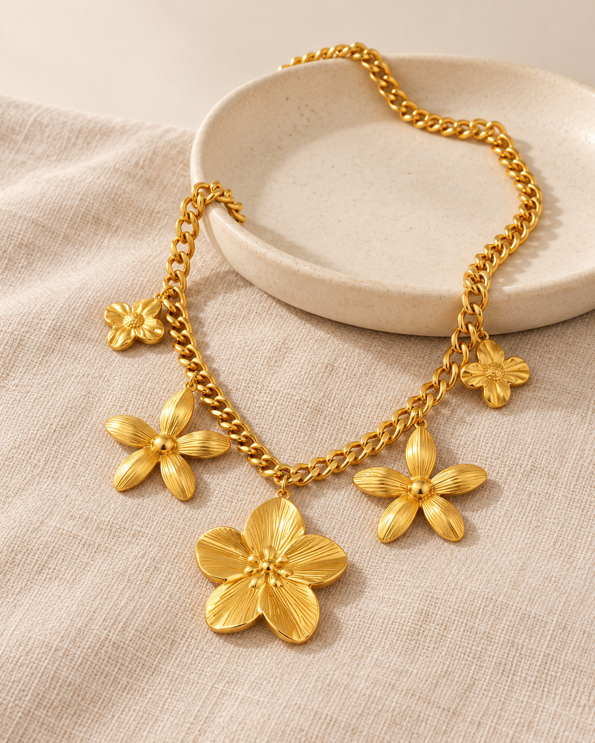 Octavie stainless steel curb chain necklace with five flower charms in Gold, still life on linen